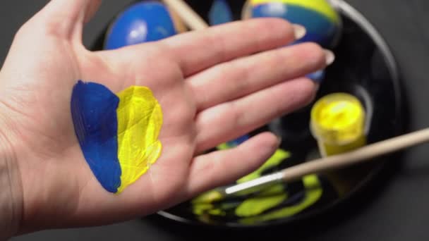 Geschilderde vrouwelijke hand in geel-blauwe kleur op de achtergrond van paaseieren — Stockvideo