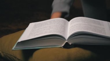 Sevimli kız, yatakta rahat bir şekilde yatarken kitap okuyup sayfalarını karıştırıyor.