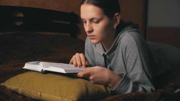 Schattig meisje leest en blaadjes door middel van een boek terwijl liggend comfortabel in bed — Stockvideo