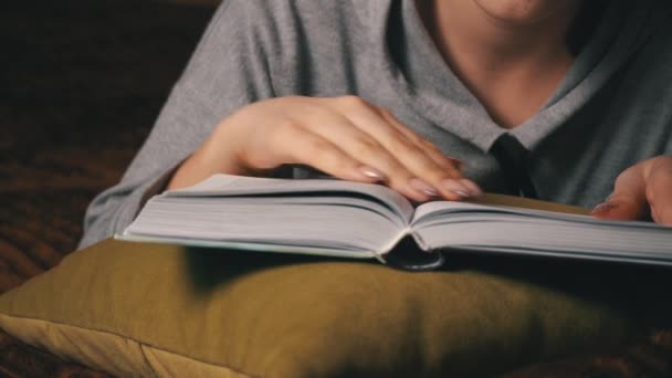 Χαριτωμένο κορίτσι διαβάζει και φύλλα μέσα από ένα βιβλίο, ενώ βρίσκεται άνετα στο κρεβάτι — Αρχείο Βίντεο