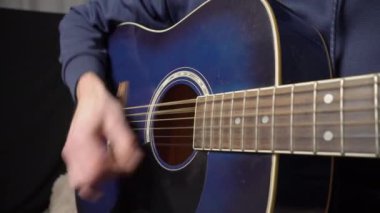 Adam koltukta otururken akustik gitar çalıyor.
