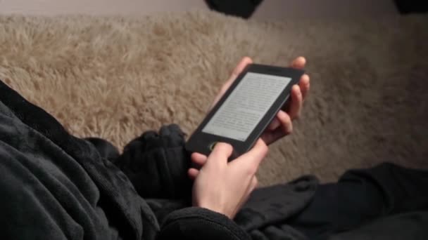 Чоловік у халаті читає електронну книгу сидячи на дивані — стокове відео