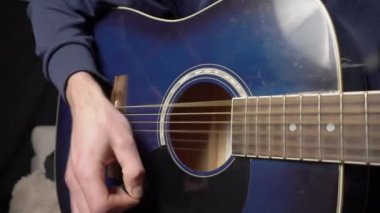 Adam koltukta otururken akustik gitar çalıyor.