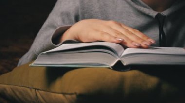 Sevimli kız, yatakta rahat bir şekilde yatarken kitap okuyup sayfalarını karıştırıyor.