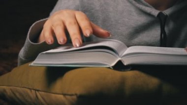 Sevimli kız, yatakta rahat bir şekilde yatarken kitap okuyup sayfalarını karıştırıyor.