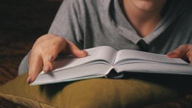 Sevimli kız, yatakta rahat bir şekilde yatarken kitap okuyup sayfalarını karıştırıyor.