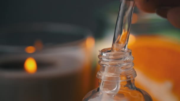 Etherische olie druppelt van een pipet in een fles op de achtergrond van een kaars — Stockvideo