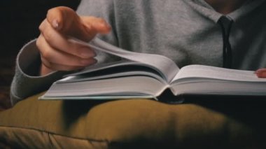 Sevimli kız, yatakta rahat bir şekilde yatarken kitap okuyup sayfalarını karıştırıyor.