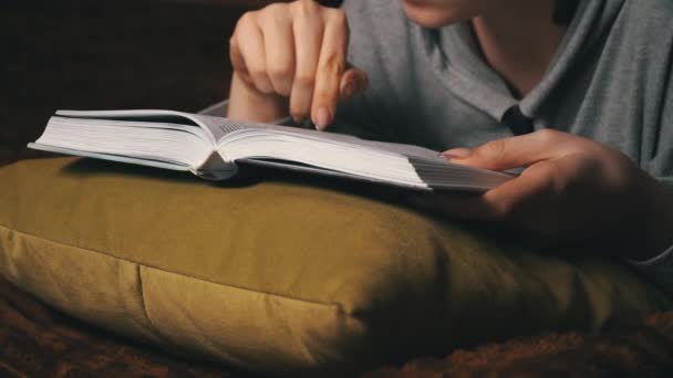 Linda chica lee y hojas a través de un libro mientras está acostado cómodamente en la cama — Vídeos de Stock