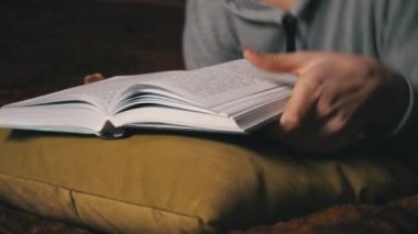 Sevimli kız, yatakta rahat bir şekilde yatarken kitap okuyup sayfalarını karıştırıyor.