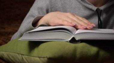 Güzel kız yatakta yatarken rahatça kitap okur.