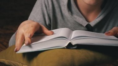 Sevimli kız, yatakta rahat bir şekilde yatarken kitap okuyup sayfalarını karıştırıyor.