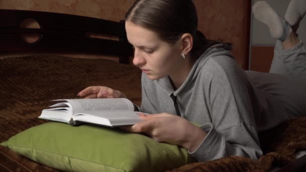 Mooi meisje leest een boek comfortabel terwijl liggend in bed — Stockvideo