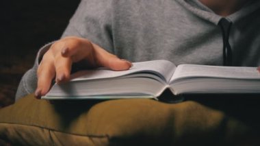 Sevimli kız, yatakta rahat bir şekilde yatarken kitap okuyup sayfalarını karıştırıyor.