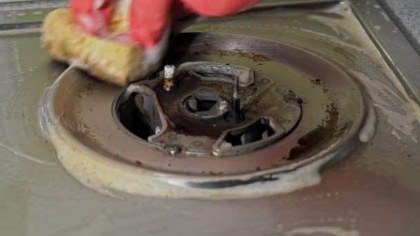 Huisvrouw in handschoenen wast het vuile oppervlak van een gasfornuis met een washandje — Stockvideo