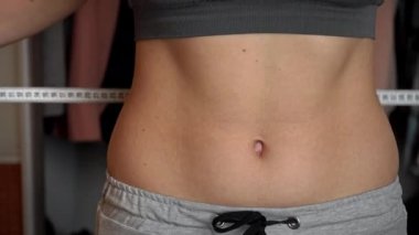 Güzel vücutlu bir kız, ölçü bandıyla belini ölçüyor.