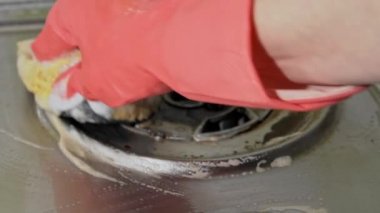 Eldivenli ev hanımı gaz sobasının kirli yüzeyini havluyla yıkıyor.