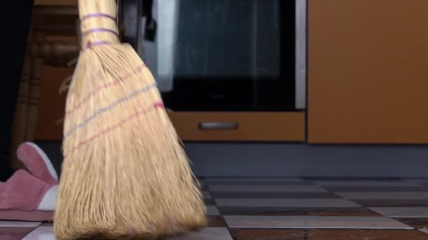 Νεαρό κορίτσι σαρώνει το πάτωμα στην κουζίνα με ένα συνηθισμένο σκούπα σε αργή Μο — Αρχείο Βίντεο