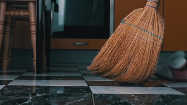 Νεαρό κορίτσι σαρώνει το πάτωμα στην κουζίνα με ένα συνηθισμένο σκούπα σε αργή Μο — Αρχείο Βίντεο