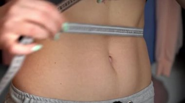 Güzel vücutlu bir kız, ölçü bandıyla belini ölçüyor.