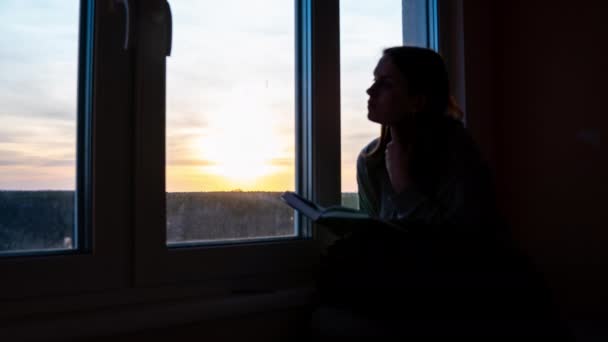 Portakal rengi gün batımına karşı kitap okuyan yalnız bir kızın zamanı. — Stok video