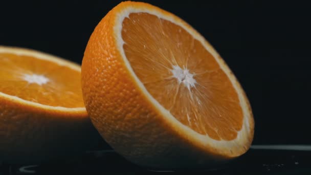 Eine halbe saftige Orange dreht sich auf schwarzem Hintergrund im Kreis — Stockvideo
