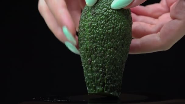 Lányok kéz tart egy avokádó vágott két részre egy fekete háttér — Stock videók