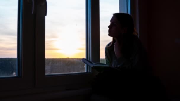 Timelapse de uma menina solitária lendo um livro contra o pano de fundo do pôr-do-sol laranja — Vídeo de Stock
