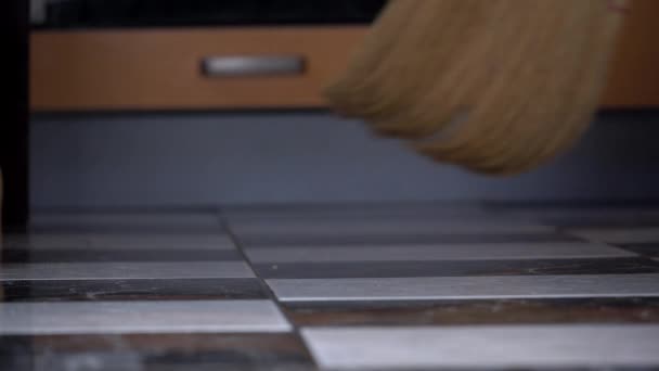 Νεαρό κορίτσι σαρώνει το πάτωμα στην κουζίνα με ένα συνηθισμένο σκούπα — Αρχείο Βίντεο