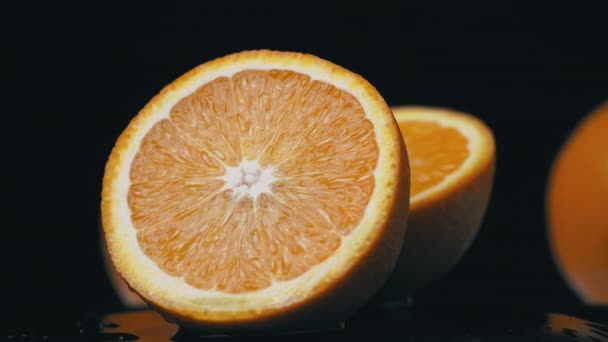 La mitad de una naranja jugosa gira en un círculo sobre un fondo negro — Vídeo de stock