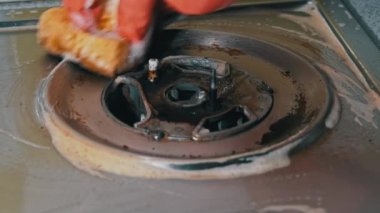 Eldivenli ev hanımı gaz sobasının kirli yüzeyini havluyla yıkıyor.