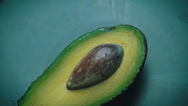 La mitad de un aguacate con una piedra gira en un círculo sobre un fondo negro — Vídeo de stock