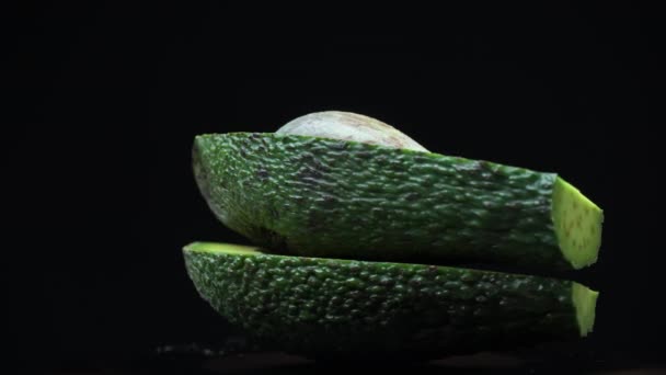 Две половинки авокадо вращаются в круге на черном фоне — стоковое видео