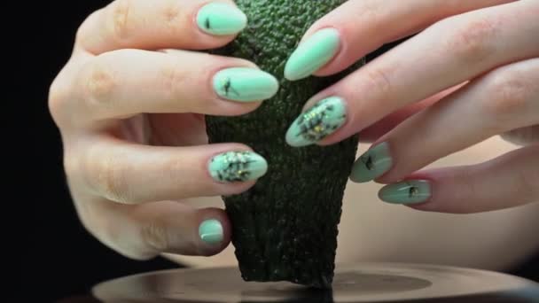 Mädchenhand hält einen Avocado-Schnitt in zwei Teile auf schwarzem Hintergrund — Stockvideo