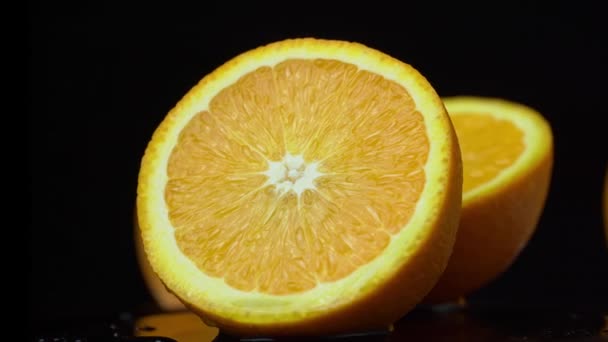 Metade de uma laranja suculenta gira em um círculo em um fundo preto — Vídeo de Stock