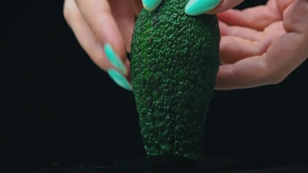 Mão de meninas segura um corte de abacate em duas partes em um fundo preto — Vídeo de Stock