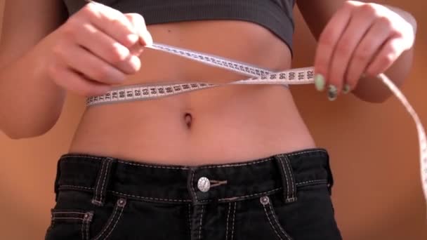 Flicka med en vacker figur sätta på gamla stora jeans och mäter hennes midja — Stockvideo