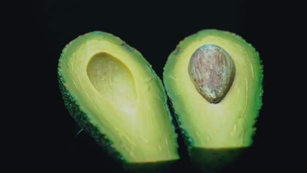 Dos mitades de un aguacate giran en un círculo sobre un fondo negro — Vídeo de stock