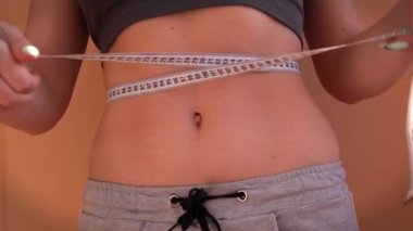 Güzel vücutlu bir kız, ölçü bandıyla belini ölçüyor.