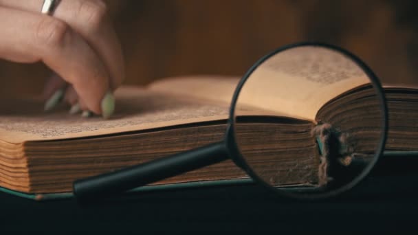 Girl Turns the Page of an Old Book Next to a Magnifying Glass — Stock Video