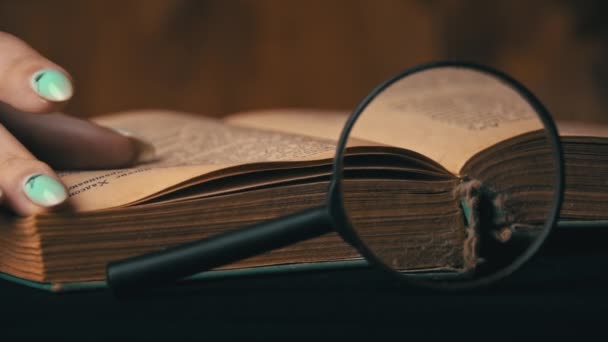 Girl Turns the Page of an Old Book Next to a Magnifying Glass — Stock Video