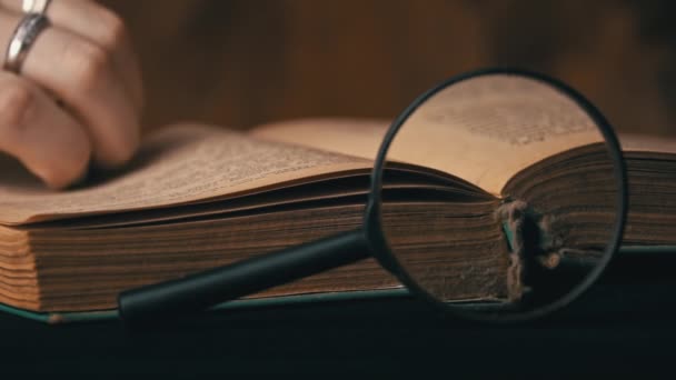 Ragazza gira la pagina di un vecchio libro accanto a una lente d'ingrandimento — Video Stock