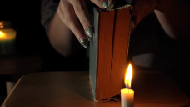 Dziewczyna przy świecach Otwiera i czyta starą książkę w godzinach wieczornych — Wideo stockowe