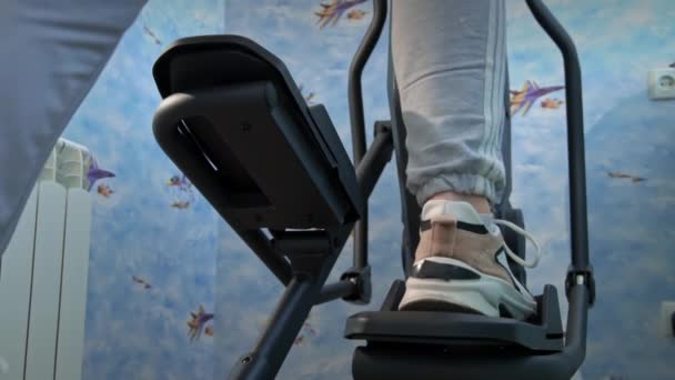 Chica joven en zapatillas de deporte se involucra en un orbitrek en casa, Vista inferior — Vídeos de Stock