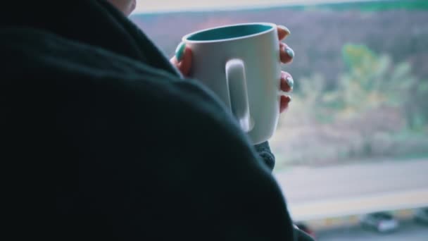 Женщина пьет кофе из чашки в черном халате на открытом окне утром — стоковое видео