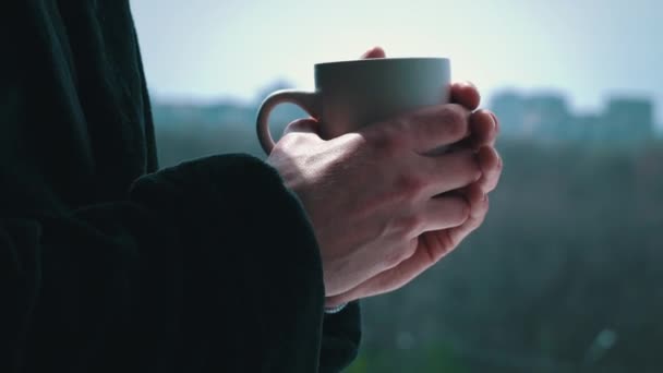 Man drinkt koffie uit beker in zwarte badjas bij een open raam in de ochtend — Stockvideo