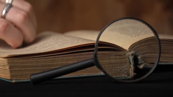 Girl Turns the Page of an Old Book Next to a Magnifying Glass — Stock Video