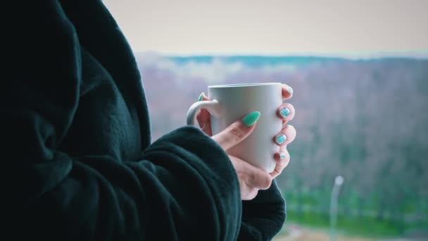 Femeia bea cafea din ceașcă în halat de baie negru la o fereastră deschisă dimineața — Videoclip de stoc