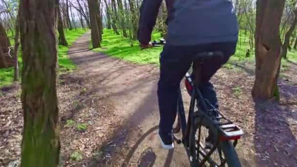 Nuori kaveri ajaa polkupyörää pitkin polkua vihreässä metsässä, takana näkymä hitaaseen Mo — kuvapankkivideo