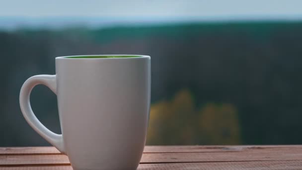 Une tasse de thé chaud ou de café se tient près d'une fenêtre ouverte et émet de la vapeur — Video